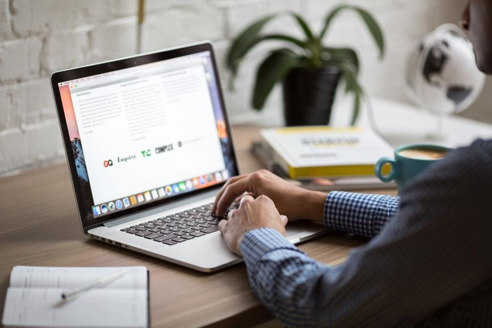 A person working at a laptop with a notebook and coffee