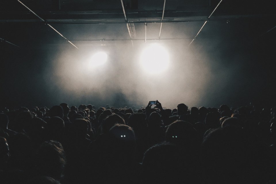 A crowd facing a brightly lit stage at an indoor concert